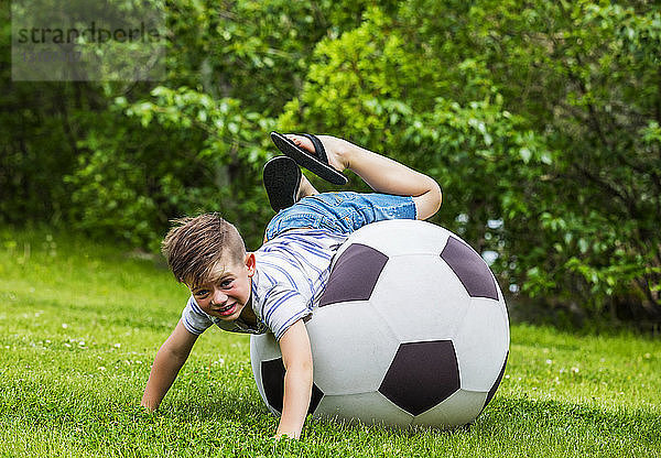 Ein kleiner Junge stürzt beim Spielen in einem Park an einem warmen Sommertag vom Rand eines großen Balls; Edmonton  Alberta  Kanada