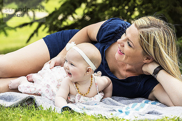 Eine junge Mutter spielt mit ihrem Baby auf einer Decke in einem Stadtpark an einem warmen Sommertag; Edmonton  Alberta  Kanada