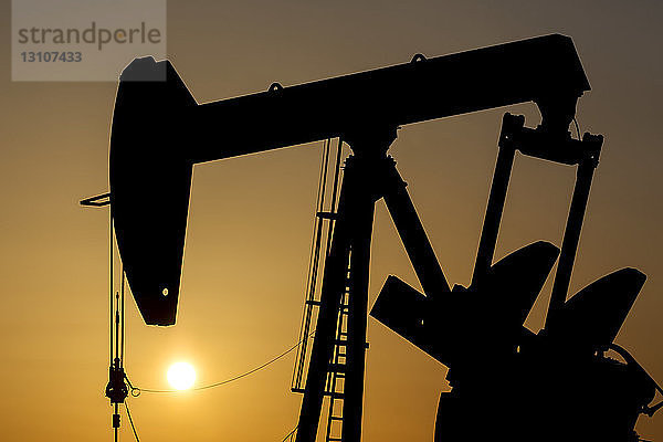 Silhouette eines Pumpjacks bei Sonnenaufgang mit einem glühend warmen Himmel  westlich von Airdrie; Alberta  Kanada