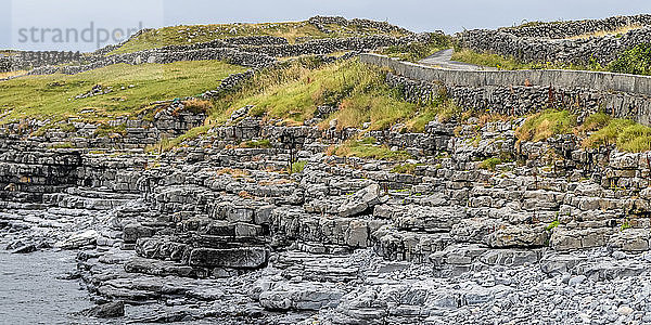 Steinmauern und eine Straße entlang der Küste von Inishmore  der größten der Aran-Inseln  Irland; Kilronan  Grafschaft Galway  Irland