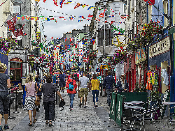 Belebtes Einkaufsviertel mit vielen Fußgängern und Geschäften  über denen internationale Flaggen hängen; Galway  County Galway  Irland