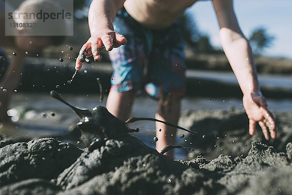 Ausgeschnittenes Bild von Brüdern  die am Strand im Schlamm spielen