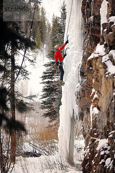 Niedrigwinkelansicht eines Wanderers  der an einem gefrorenen Wasserfall gegen eine Felsformation klettert