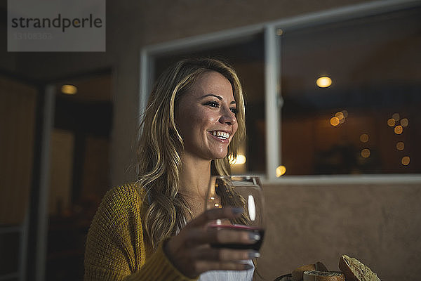 Lächelnde Frau mit Weinglas schaut weg  während sie auf der Terrasse steht