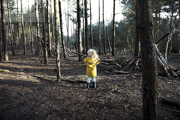 Rückansicht eines spielerischen Mädchens mit Stock im Wald