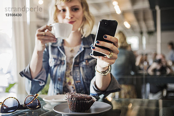 Frau hält Smartphone in der Hand  während sie im Cafe steht
