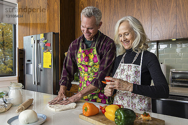 Lächelnde Frau schneidet Paprika  während der Mann zu Hause in der Küche Pizzateig macht