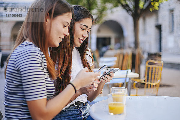 Freunde benutzen Mobiltelefone  während sie im Straßencafé sitzen