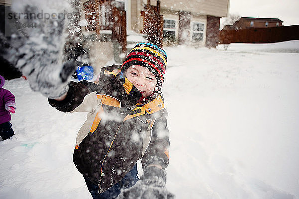 Porträt eines glücklichen Jungen  der im Hof mit Schnee spielt