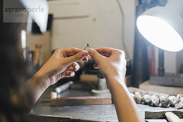 Geschorene Hände einer Handwerkerin  die in der Werkstatt einen Ring am Tisch hält