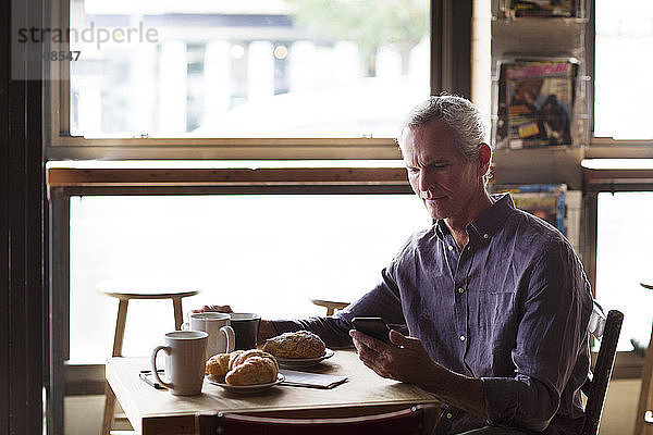 Erwachsener Mann telefoniert bei Croissants und Kaffee am Tisch im Café