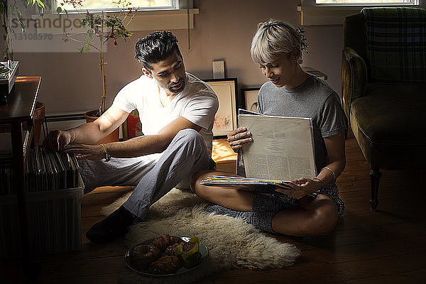 Junges Paar wählt Vinyl-Schallplatten  während es zu Hause auf dem Boden sitzt