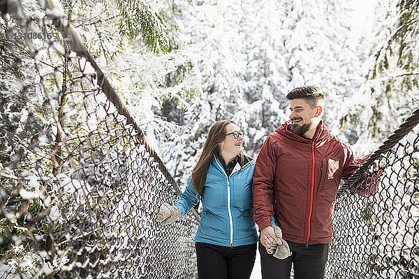 Lächelndes Paar geht im Winter auf einer Fußgängerbrücke mitten im Wald im Lynn Canyon Park