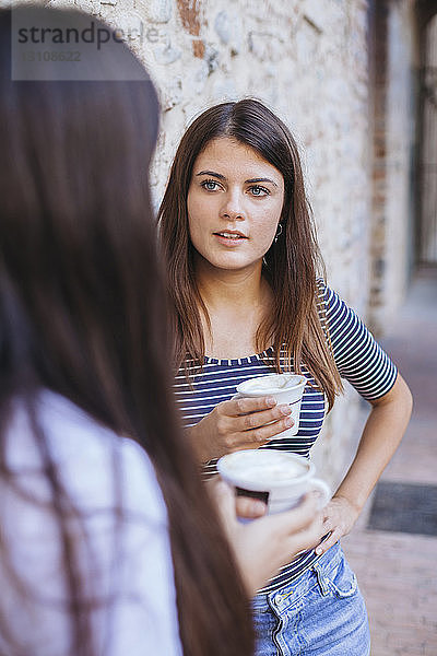 Freunde halten Kaffeetassen in der Hand und unterhalten sich  während sie an einer Ziegelmauer stehen