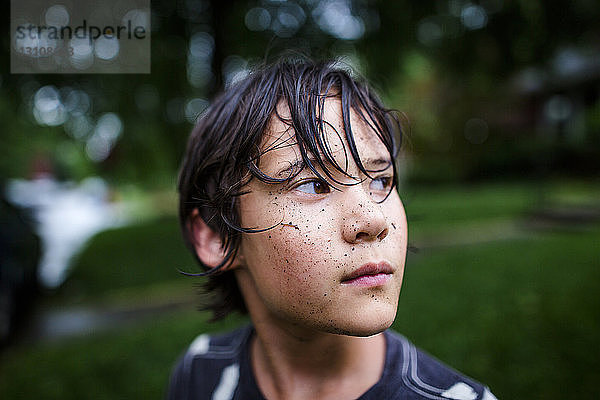 Nahaufnahme eines nachdenklichen Jungen mit schmutzigem Gesicht  der während der Regenzeit im Hof steht