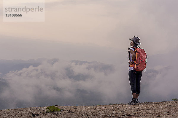Seitenansicht einer Wanderin mit Rucksack  die bei nebligem Wetter auf dem Berg steht