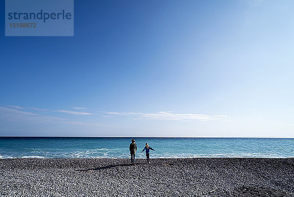 Rückansicht einer älteren Frau  die mit einem Mädchen am Strand gegen den Himmel steht