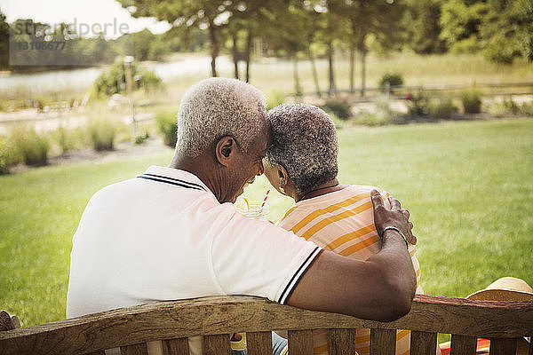 Rückansicht eines romantischen Seniorenpaares auf einer Parkbank sitzend