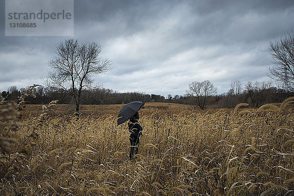 Teenagermädchen mit Regenschirm steht auf Feld gegen Gewitterwolken