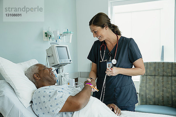 Lächelndes Händeschütteln der Krankenschwester mit einem älteren Patienten  der auf der Krankenhausstation auf dem Bett liegt