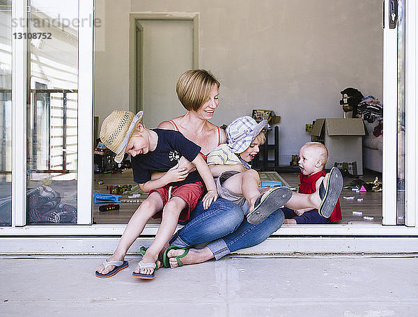 Mutter spielt mit Kindern  während sie zu Hause auf der Türschwelle sitzt
