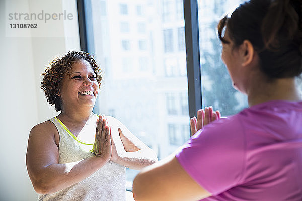 Glückliche Freunde mit gefalteten Händen üben von Angesicht zu Angesicht im Yoga-Studio