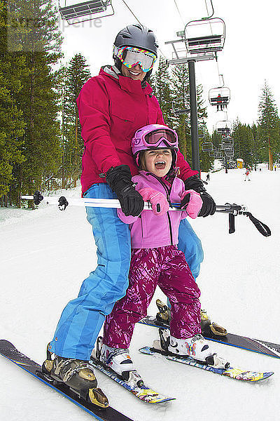 Glückliche Mutter und Mädchen beim Skifahren auf schneebedecktem Feld
