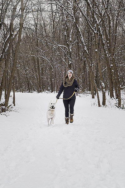 Glückliche Frau geht mit Hund auf schneebedecktem Feld gegen kahle Bäume