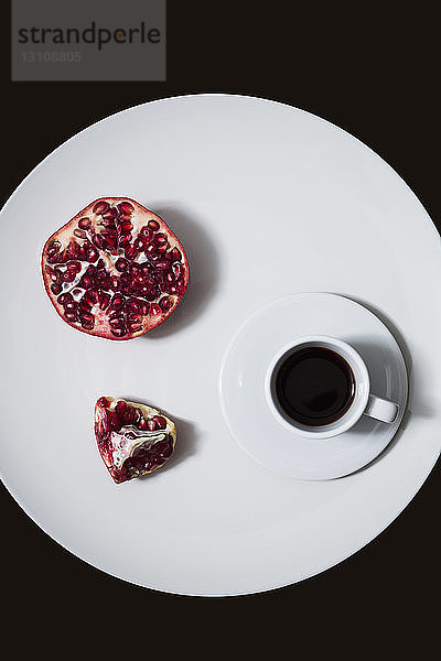 Draufsicht auf Kaffee mit Granatapfel im Teller über schwarzem Hintergrund