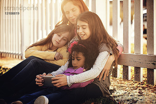 Familie benutzt Smartphone  während sie am Zaun im Hinterhof sitzt