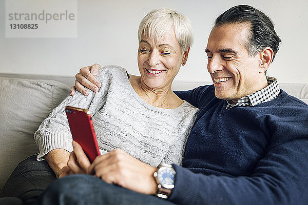 Älteres Ehepaar betrachtet Smartphone  während es zu Hause auf dem Sofa sitzt
