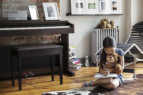 Mädchen schreibt in Buch  während sie zu Hause auf dem Teppich sitzt