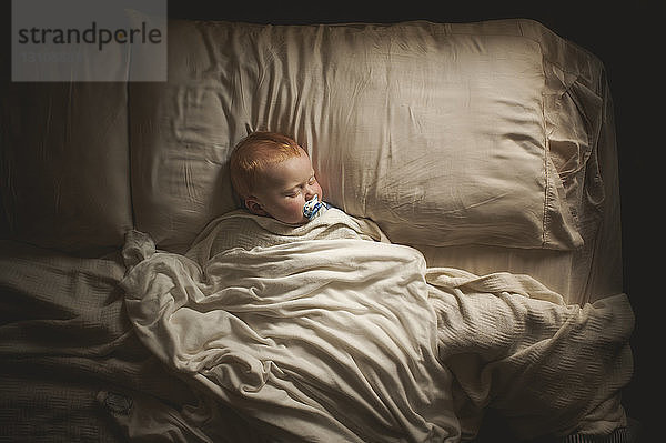 Draufsicht auf einen kleinen Jungen  der am Schnuller nuckelt  während er im Bett schläft