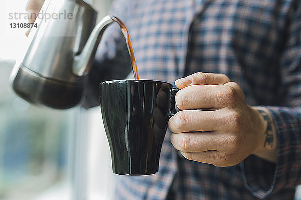 Ein Mann gießt zu Hause Kaffee in eine Tasse