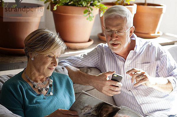 Älteres Ehepaar schaut sich Zeitschrift an  während es auf dem Sofa sitzt