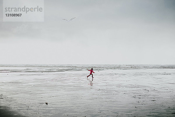 Mitteldistanz eines Mädchens  das am Strand gegen den Himmel läuft