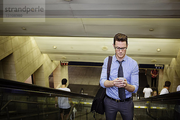 Geschäftsmann benutzt Smartphone  während er auf der Rolltreppe in der U-Bahn-Station steht