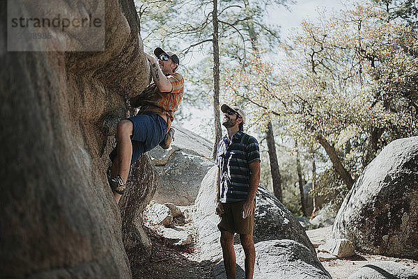 Mann schaut Freund beim Klettern am Fels an  während er im Wald steht