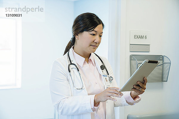 Ärztin schaut auf Tablet-Computer  während sie im Krankenhauskorridor steht