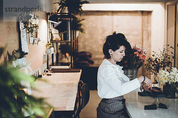 Seitenansicht eines Floristen  der Blumenschäume bei Tisch im Blumengeschäft schneidet