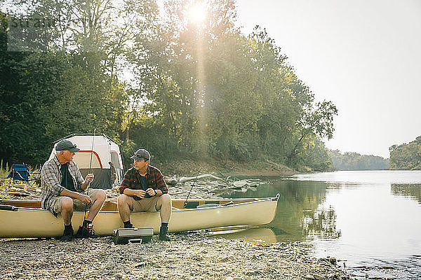 Freunde mit Angelruten unterhalten sich  während sie auf einem Boot auf dem Campingplatz sitzen