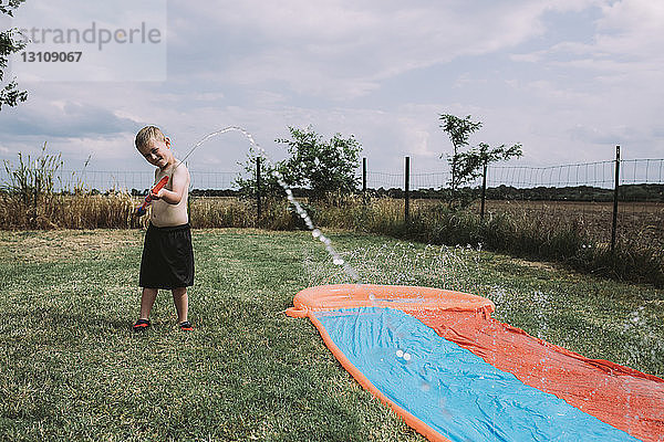 Junge spielt mit Spritzpistole an Wasserrutsche im Hof