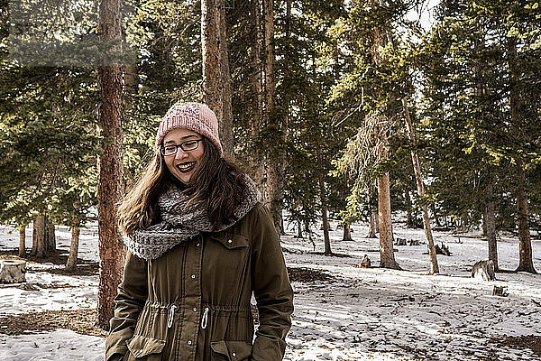 Fröhliche Frau trägt warme Kleidung  während sie im Winter im Wald steht