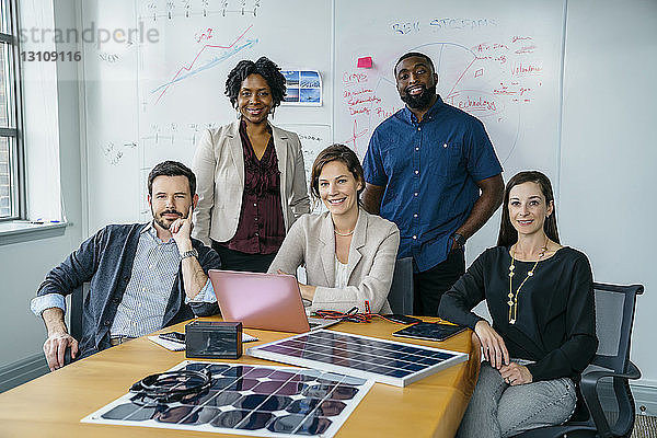 Porträt von lächelnden Geschäftsleuten durch Solarpanel-Modelle auf dem Schreibtisch
