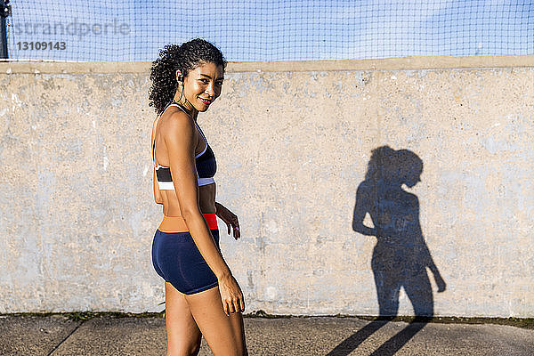 Porträt einer Sportlerin  die sich im Stehen auf einem Fußweg an der Wand bewegt