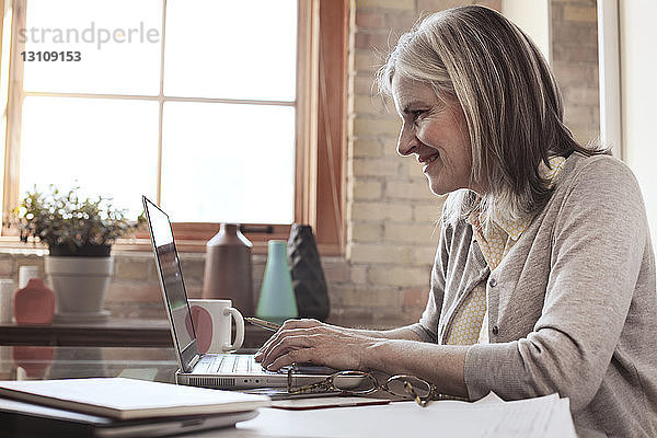 Seitenansicht einer lächelnden Geschäftsfrau mit Laptop im Kreativbüro