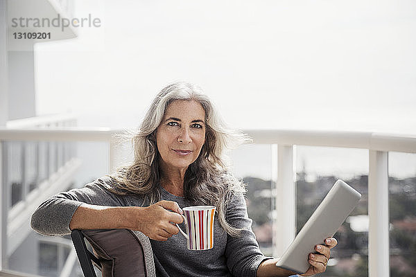 Porträt einer selbstbewussten reifen Frau mit Tablet-Computer und Kaffeetasse auf dem Balkon