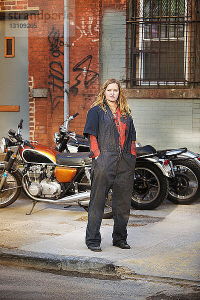 Nachdenkliche Mechanikerin steht vor der Werkstatt gegen Fahrräder