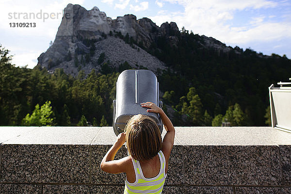 Rückansicht eines Mädchens  das durch ein Teleskop auf das Mount Rushmore National Memorial blickt