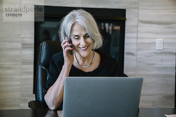Lächelnde Geschäftsfrau beantwortet Smartphone  während sie im Büro sitzt